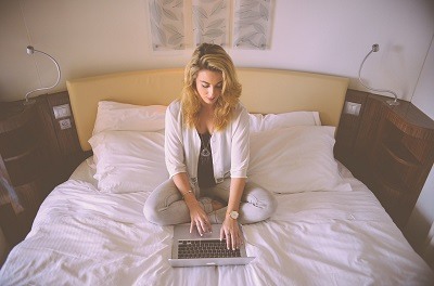 pretty young woman sitting in her bed using her laptop