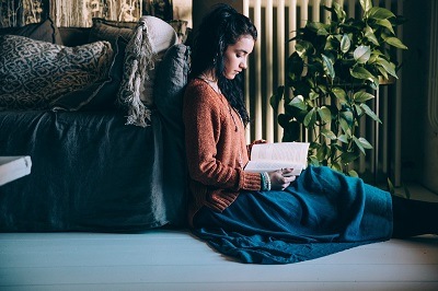 young girl leaning against a sofa and is reading a book